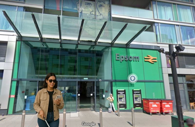 Visually impaired lady with smartphone app outside Epsom Railway station - background - Google Maps